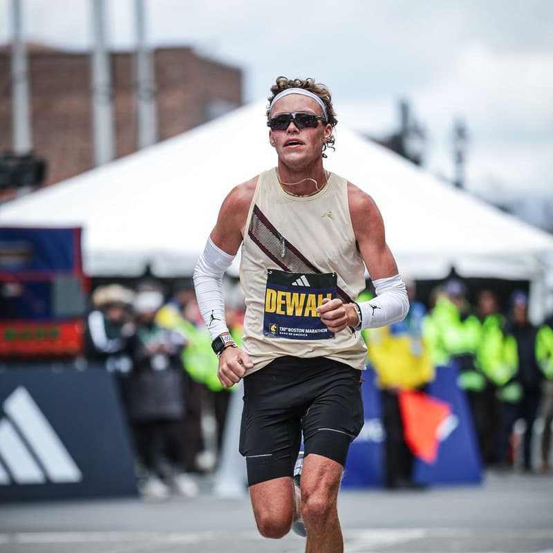 Lars Dewall in a cream singlet, headband and dark sunglasses running toward the camera at the Boston Marathon.