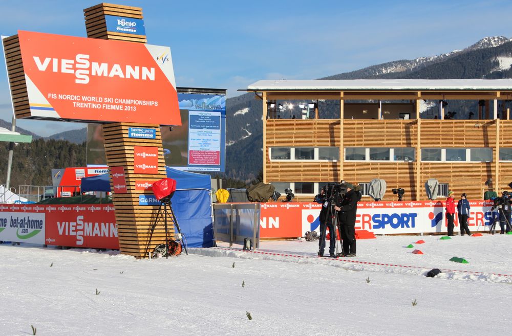 TV personnel fine-tune near the finish line. The wood building behind them was built specifically for television media at the 2013 FIS Nordic World Ski Championships at the Lago di Tesero stadium in Val di Fiemme, Italy.