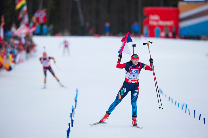 Olga Vilukhina skis across the finish line with the Russian flag, as Franziska Hilebrand (GER) skis it in for second place.  Photo: Fischer / Nordic Focus.