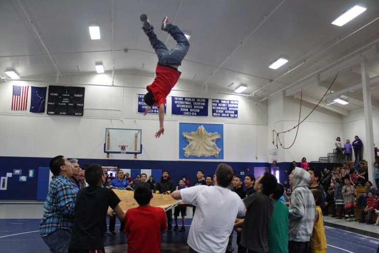 A student is thrown into the air as part of the traditional blanket toss - using a walrus hide - in the school gym in Gambell. (Photo: Skiku)