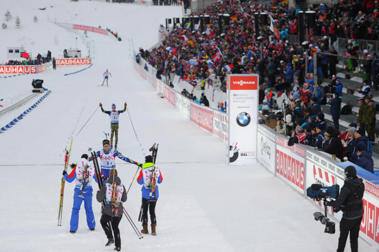 France’s Martin Fourcade is greeted by his teammates after winning gold in the mixed relay to open the 2016 Biathlon World Championships in Oslo, while behind him Germany’s Simon Schempp crosses the finish line for the silver medal, and Norway’s Tarjei Bø comes onto the final stretch to claim bronze. (Photo: IBU/Evgeny Tumashov)