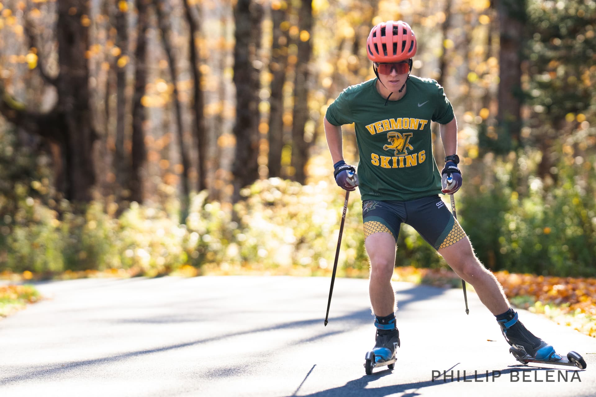A University of Vermont skier rollerskiing on a paved road lined with fall foliage at Craftsbury, Vermont