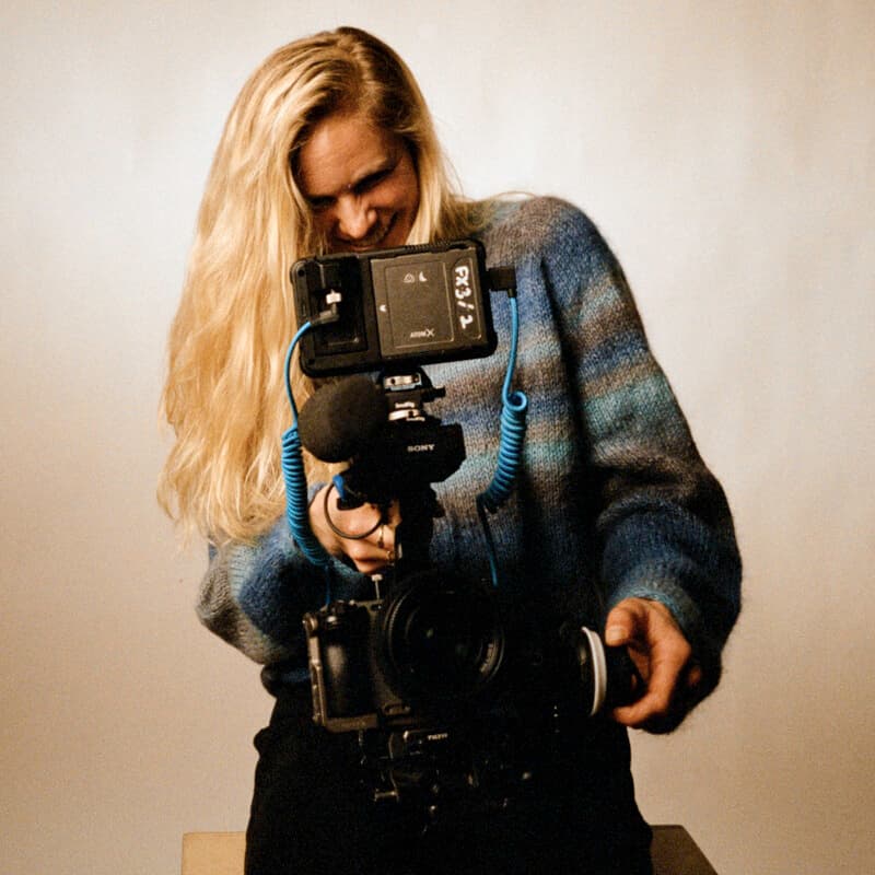 Jessie Diggins smiling as she holds a Sony cinema camera rig in front of a plain backdrop.