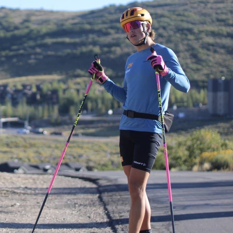 Johannes Høsflot Klæbo standing on rollerskis in a blue top, yellow helmet and pink poles on a road in Park City, Utah