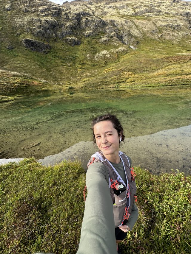 Kendall Kramer in a running vest above an alpine lake in the Alaska mountains.
