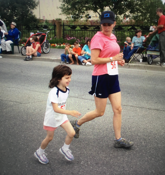 A young Kendall Kramer running a road race alongside an adult runner wearing a race bib.